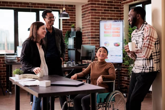 Woman sitting in a wheelchair in an office surrounded by smiling colleagues