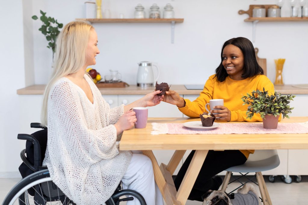 A woman in a wheelchair sharing a muffin with another woman